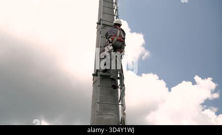Ouvrier grimpant au poteau portant un harnais de sécurité en hauteur Banque D'Images