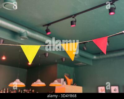 Drapeaux triangulaires colorés de fanion suspendus à l'intérieur du café. Célébration, joie et design joyeux dans un espace public festif. Banque D'Images