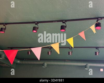 Drapeaux triangulaires colorés de fanion suspendus à l'intérieur du café. Célébration, joie et design joyeux dans un espace public festif. Banque D'Images