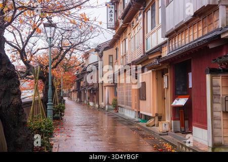 Vue sur la rue calme avec des bâtiments traditionnels en bois et des feuilles d'automne dispersées sur le trottoir humide, Kanazawa, Ishikawa, Japon. Banque D'Images