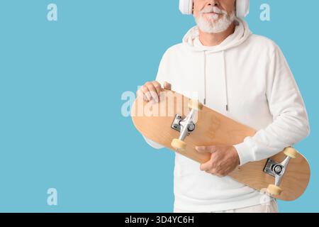 Homme senior dans des écouteurs avec skateboard sur fond bleu Banque D'Images