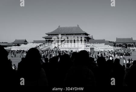 À l’intérieur de la Cité interdite, vue en noir et blanc des foules qui s’écoulent vers le hall principal, encadrée par l’ombre de la passerelle Banque D'Images