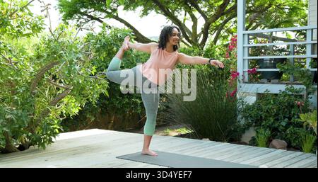 Femme en équilibre dans le haut de saumon, leggings gris effectuant le yoga sur le pont avec tapis gris, tracker de poignet Banque D'Images