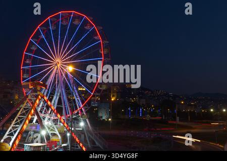 Un cliché de nuit saisissant avec une grande roue éclairée décorée de lumières rouges et bleues fluo. La roue domine le cadre gauche contre un sombre Banque D'Images
