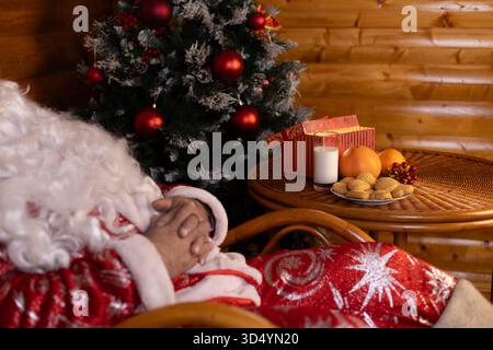 Père Noël assis dans une chaise, tenant une bougie, à côté de l'arbre de Noël Banque D'Images