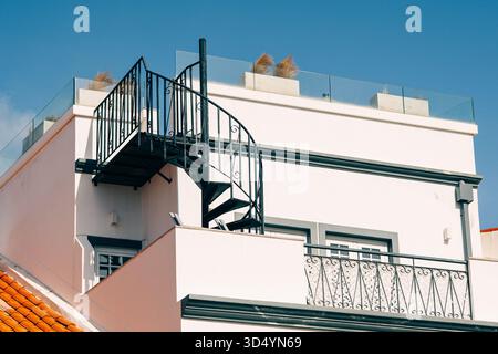 Un bâtiment blanc moderne dispose d'un toit-terrasse accessible par un escalier en colimaçon en métal noir sous un ciel bleu clair. Banque D'Images