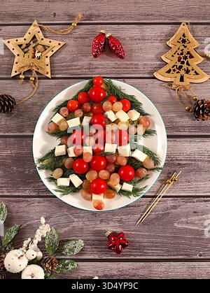 Plats de Noël et du nouvel an, salade de vacances traditionnelle sous la forme d'un arbre de Noël comestible vivant avec du fromage feta, des olives, des tomates et des raisins, Banque D'Images