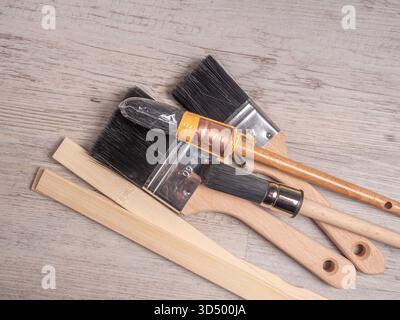 Une grappe de pinceaux à manche en bois assortis et de bâtons mélangeurs repose sur une surface en bois clair. Banque D'Images