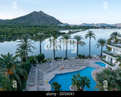 Vue aérienne sur la piscine d'un centre de villégiature avec chaises longues, palmiers, lac et grande montagne en toile de fond. Banque D'Images