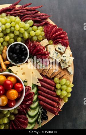 Une belle planche de fromage et de charcuterie comprend un assortiment de fromages, charcuteries, raisins, olives, tomates cerises, et les crackers, idéaux pour les événements ou les événements occasionnels Banque D'Images