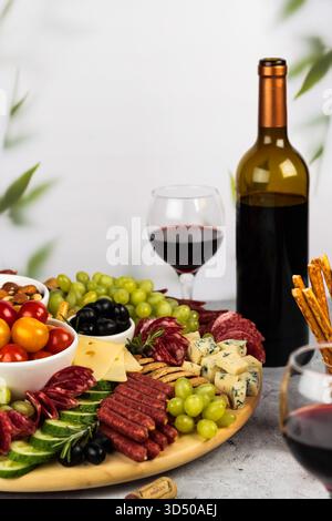 Une planche de charcuterie colorée présente une variété de viandes, fromages et fruits frais soigneusement disposés. Banque D'Images