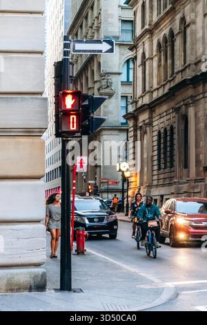 Montréal, Canada - 11 août 2025 : scène de rue au centre-ville de Montréal avec feux de circulation, cyclistes, piétons et bâtiments historiques Banque D'Images