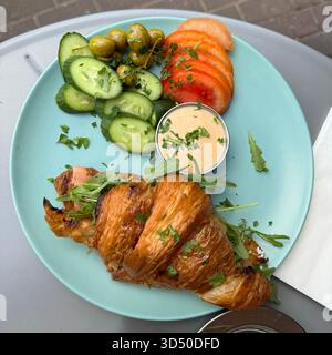 Une photo au-dessus d'un savoureux petit déjeuner servi sur une assiette turquoise vif, avec un croissant rempli de saumon et roquette, tranches de concombre, toma Banque D'Images