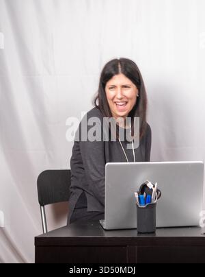 Belle femme brune rit de tout cœur lors d'une pause du travail devant le PC. La femme a trente-cinq ans, porte un pull gris et l'est Banque D'Images