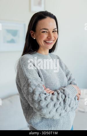 Femme debout et souriante avec les bras pliés dans le salon avec art abstrait et canapé Banque D'Images