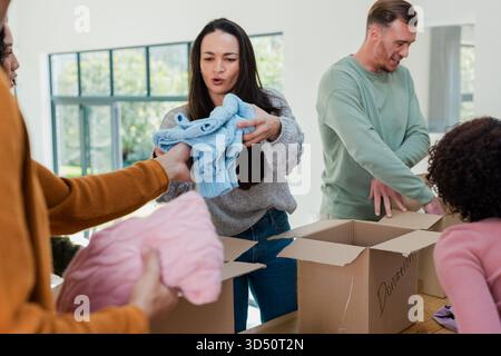 Divers bénévoles trient et emballent des chandails dans des boîtes de dons à table dans la salle communautaire Banque D'Images