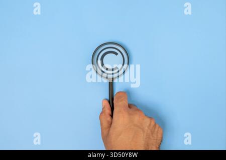 Gros plan d'une main tenant une loupe mettant l'accent sur un symbole de copyright. Concept de protection de la propriété intellectuelle, des marques et des droits créatifs Banque D'Images