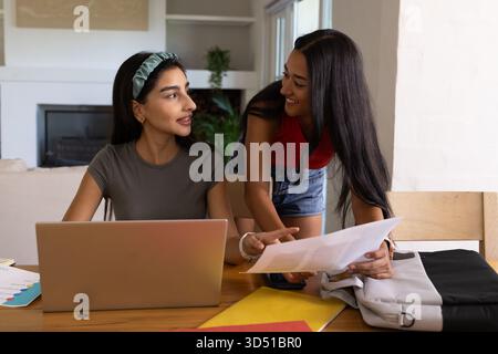 Collaborer diverses amies féminines étudiant à la table à manger à la maison, avec ordinateur portable et papiers imprimés Banque D'Images