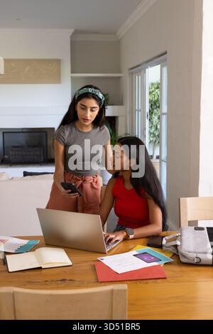 Collaborer diverses amies féminines travaillant à la table à manger à la maison, avec ordinateur portable et smartphone Banque D'Images