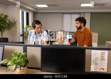 Pencher divers collègues collaborant autour de la zone de cubicule dans un bureau ouvert, avec des moniteurs Banque D'Images