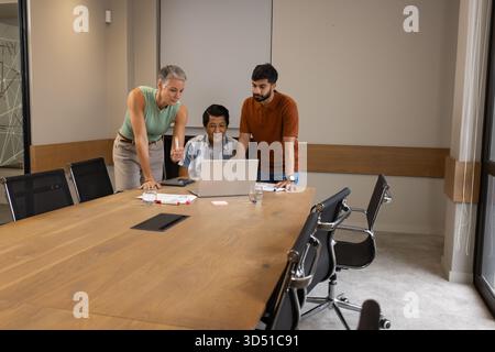 Collaboration de divers collègues penchés sur un ordinateur portable à la table de réunion avec des documents et un smartphone Banque D'Images
