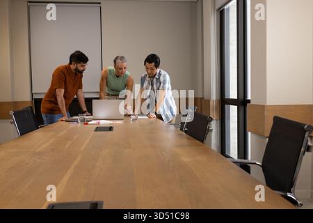 Divers collègues discutent des détails du projet dans la salle de réunion autour de l'ordinateur portable, avec des papiers et des stylos Banque D'Images
