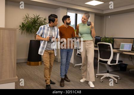 Promenez-vous entre collègues en discutant dans un espace de bureau ouvert, avec des tasses à café et une tablette Banque D'Images