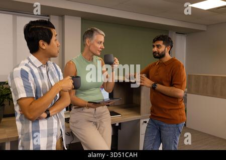 Des collègues différents discutant d'idées autour du bureau dans la salle de pause, avec des tasses à café et une tablette Banque D'Images