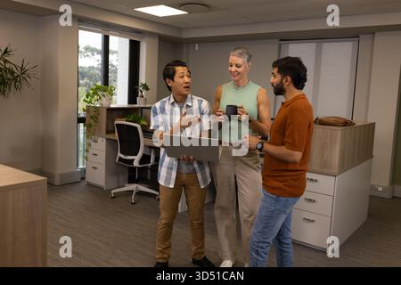 Divers collègues discutant du projet tout en se tenant debout dans le bureau, avec un smartphone tasse à café portable Banque D'Images