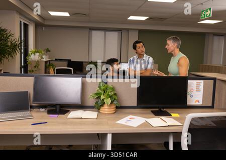 Discuter des plans divers collègues collaborant autour du bureau dans un bureau ouvert avec des écrans et des graphiques Banque D'Images