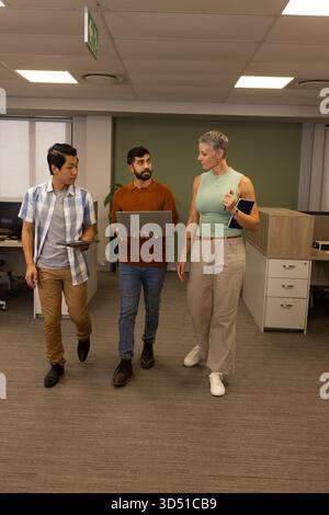 Marchant divers collègues discutant dans le couloir du bureau, avec un ordinateur portable tablette bloc-notes smartphone Banque D'Images