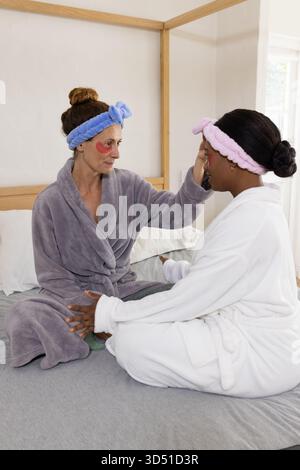 Application crème diverses amies féminines assises sur le lit, portant des bandeaux, des patchs pour les yeux Banque D'Images