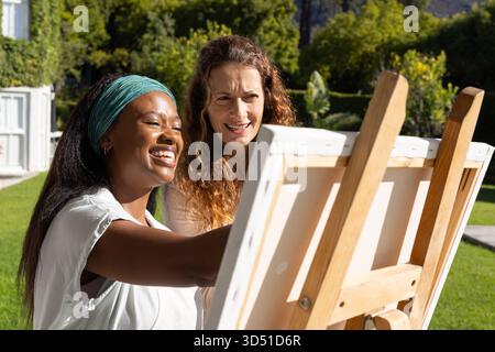 Collaboration de diverses amies peignant dans le jardin ensoleillé, avec chevalet en bois et pinceaux Banque D'Images