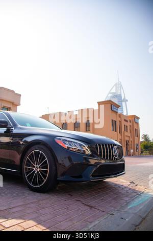 Dubaï, Émirats arabes Unis - 13 juillet 2024 : gros plan, plan bas-angle de la calandre avant et du phare d'une berline Mercedes-Benz de classe C noire avec la Burj Al Arab Banque D'Images
