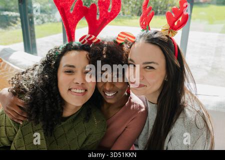 Diverses amies féminines riant et se penchant sur le canapé dans le salon portant des bandeaux en bois rouge Banque D'Images