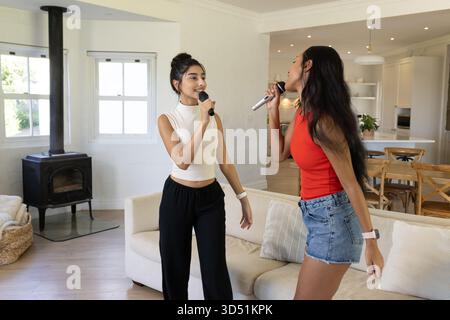 Karaoké diverses amies féminines utilisant des micros sans fil dans la cuisine ouverte, avec des coussins de canapé Banque D'Images