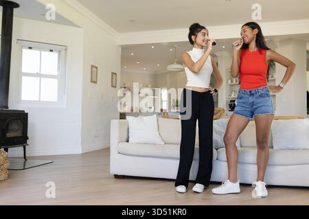Diverses amies chantant karaoké à l'aide de microphones dans la cuisine ouverte, avec cuisinière Banque D'Images