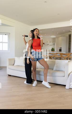 Chanter diverses amies se tenant dos à dos dans le salon, avec des microphones et un canapé Banque D'Images