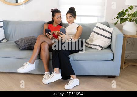 Comparaison des écrans divers amis féminins assis sur un canapé dans un salon moderne, avec des smartphones Banque D'Images