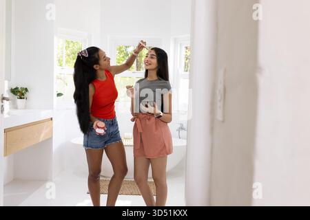 Application de maquillage divers amis féminins à l'aide d'un pinceau de maquillage dans la salle de bain à la maison, avec palette de maquillage Banque D'Images