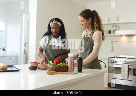 Hacher des légumes diverses amies féminines préparant la salade à l'îlot de cuisine moderne, avec de l'huile d'olive Banque D'Images