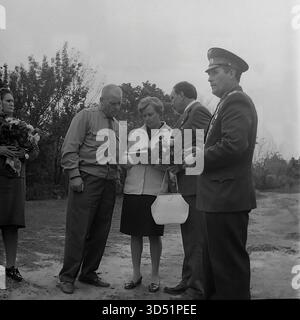 Cette photographie d'archives en noir et blanc de 1975 capture un groupe officiel et commémoratif à Sviatohirsk (alors Slavyanogorsk), en RSS d'Ukraine, lors du 30e anniversaire du jour de la victoire. La fête se tient dehors sur un chemin de terre. Le groupe comprend le vétéran aveugle Shutenko (tenant des fleurs), un officier militaire soviétique hautement décoré dans une casquette de défilé, un autre vétéran de la seconde Guerre mondiale, et leurs compagnons féminines, dont l'une tient un livre. Une jeune femme à l'extrême gauche tient également un grand bouquet. C'est un moment informel pendant les excursions de la journée. Banque D'Images
