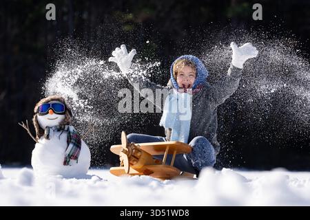 Enfant construisant un bonhomme de neige un jour d'hiver. Enfant heureux roulant de la neige pour faire un bonhomme de neige. Enfant excité jouant avec bonhomme de neige dans la neige fraîche. Banque D'Images