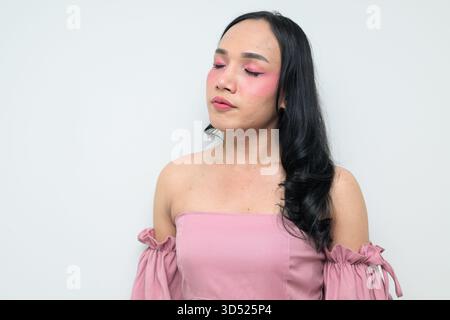 Portrait studio d'un jeune transgenre thaïlandais avec maquillage et cheveux longs. Concept d'expression de genre, fierté LGBTQ et inclusivité montrant un Banque D'Images