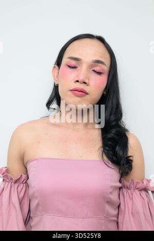 Portrait studio d'un jeune transgenre thaïlandais avec maquillage et cheveux longs. Concept d'expression de genre, fierté LGBTQ et inclusivité montrant un Banque D'Images