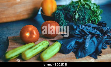 Tomates fraîches, concombres, poivrons, aneth et coriandre disposés sur une table de cuisine dans un cadre confortable, prêt à préparer un sal végétal vibrant Banque D'Images