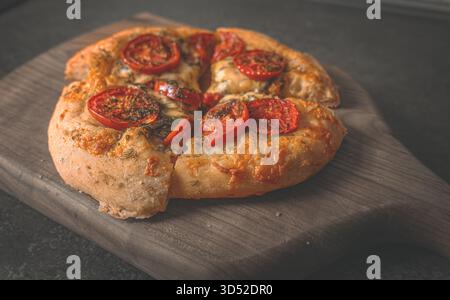 Pizza maison cuite au four avec croûte épaisse, légumes verts frais et fromage fondu sur une planche à découper en bois naturel Banque D'Images