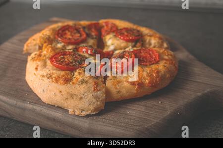 Pizza dorée et moelleuse directement sortie du four placée sur une planche de bois, garnie d'herbes aromatiques et de fromage bouillonnant Banque D'Images