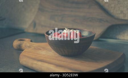Fraises juteuses dans un bol en céramique sur un comptoir de cuisine. Une lumière naturelle douce souligne la couleur vibrante et la fraîcheur des baies Banque D'Images