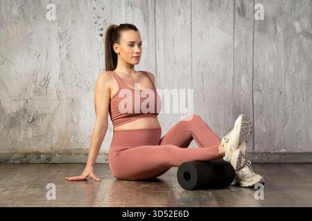 Femme enceinte effectuant un massage des mollets avec un rouleau en mousse, en se concentrant sur le bien-être prénatal Banque D'Images
